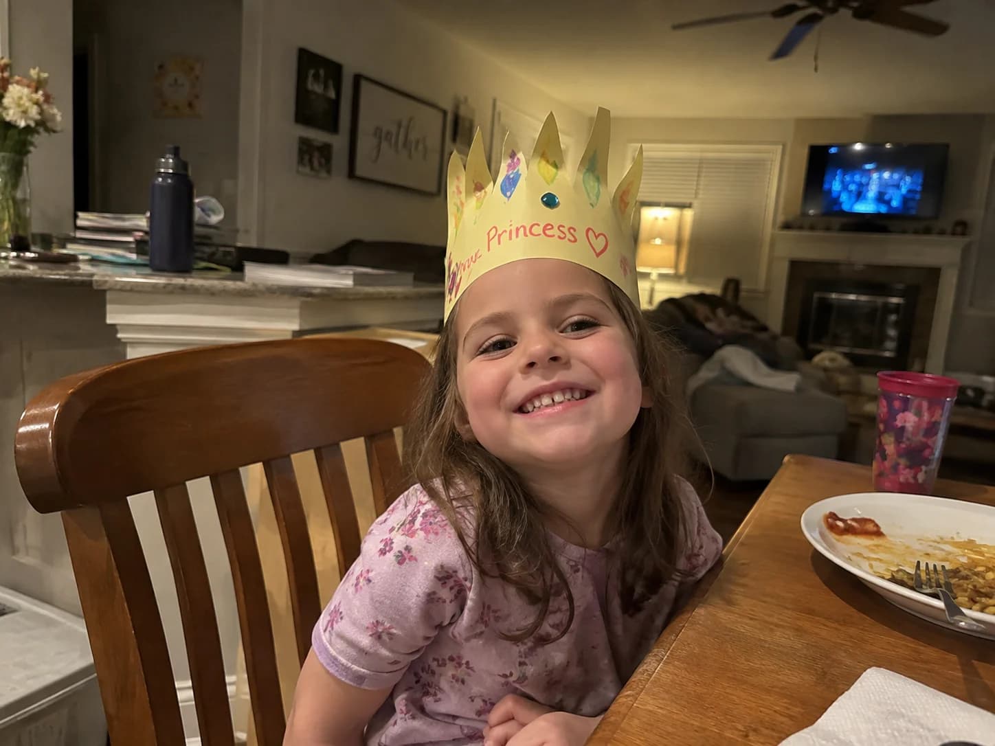 A child smiling at the dinner table in a handmade paper crown