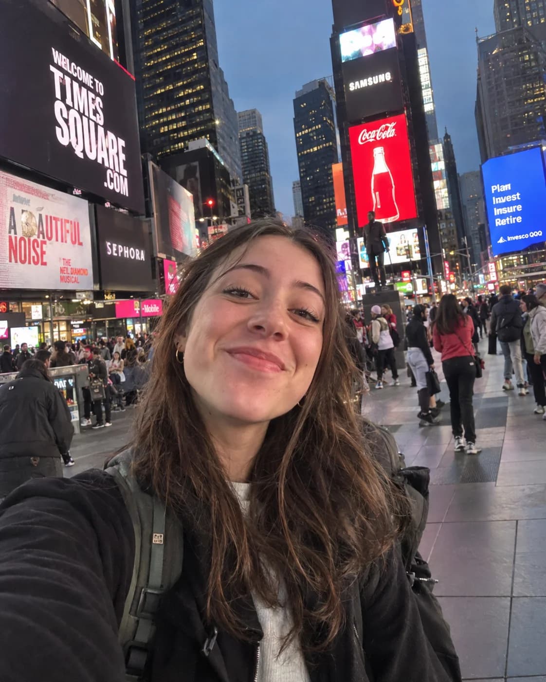 A young woman taking a selfie in Times Square at dusk